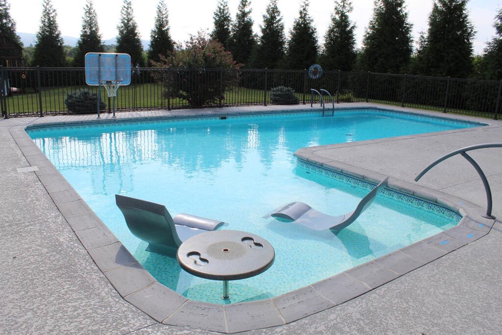 An inground pool with lounge chairs and a basketball hoop.